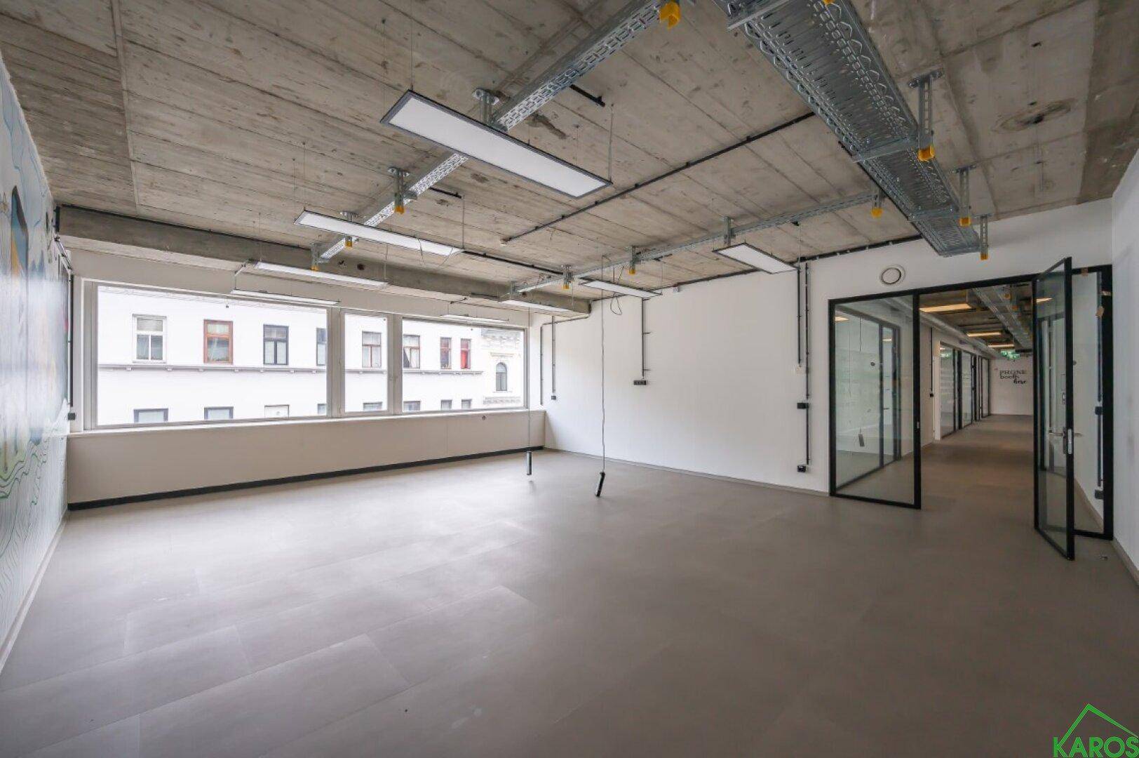 Geräumiges Büro mit langer Fensterfront, freiliegenden Leitungen und modernen Glaswänden.