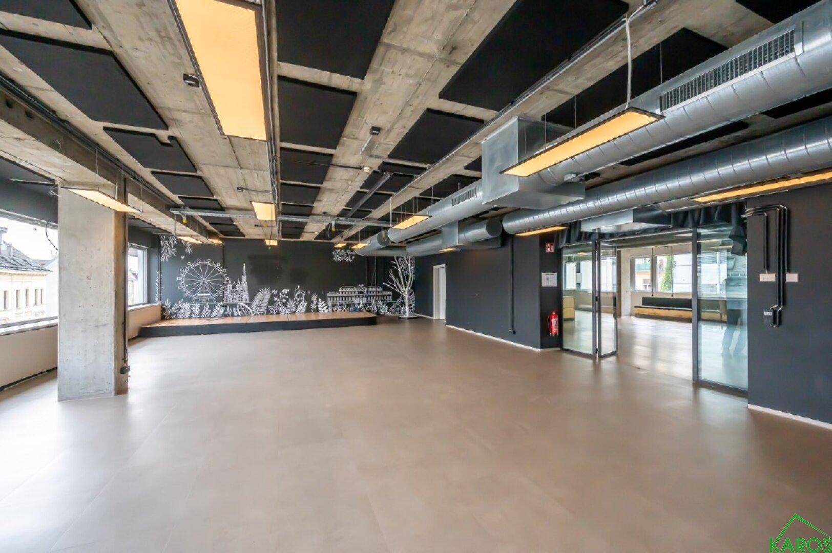 Geräumiges Büro mit Akustikdecken, freiliegenden Leitungen und einer kreativ bemalten Wand.