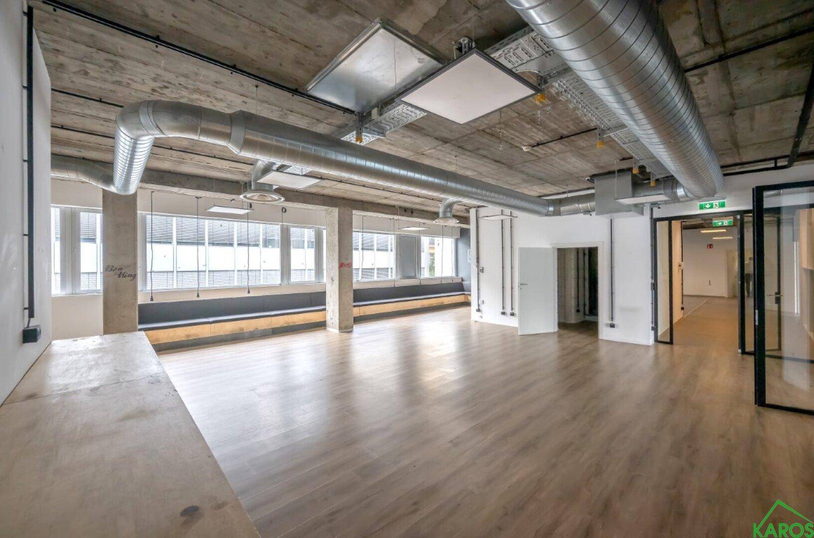 Offene Bürofläche mit Holzboden, freiliegenden Decken und einer Fensterbank mit Sitzgelegenheit.