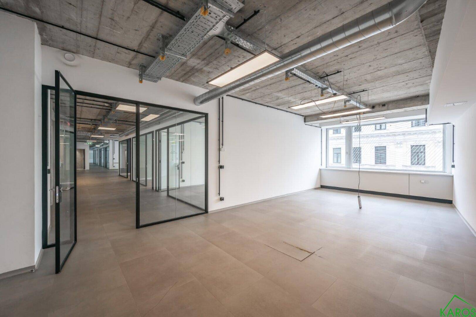 Offener Bürobereich mit Glaswänden und einer Fensterfront, die für Helligkeit sorgt.