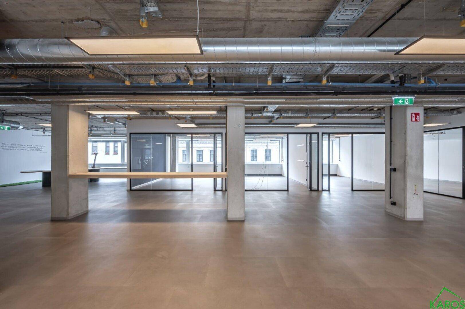 Weitläufige Bürofläche mit freiliegenden Decken, Säulen und modernen Glasabtrennungen.