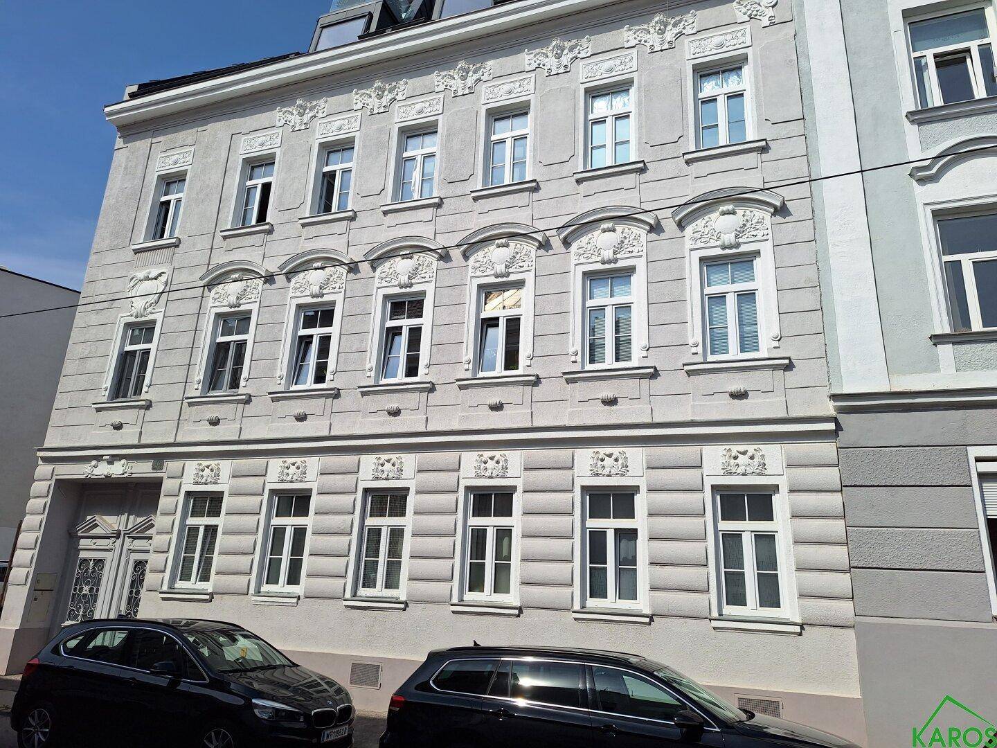 Historisches Gebäude mit einer eleganten, grau verputzten Fassade und reich verzierten Fenstern, ergänzt durch einen modernen Dachausbau.