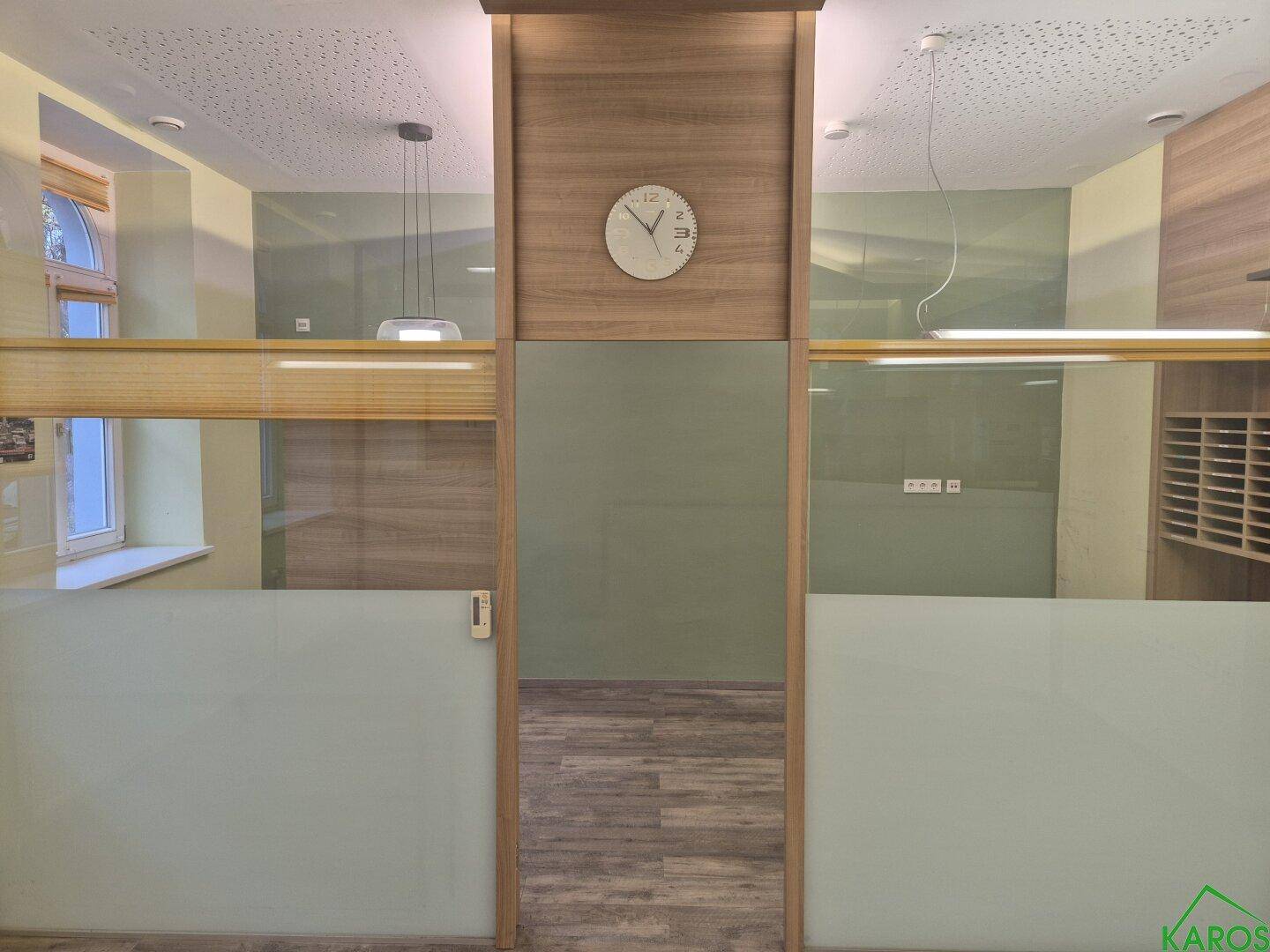 Bürobereich mit Holzelementen, Glaswänden und einer Uhr als Dekoration, bietet viel natürliches Licht.