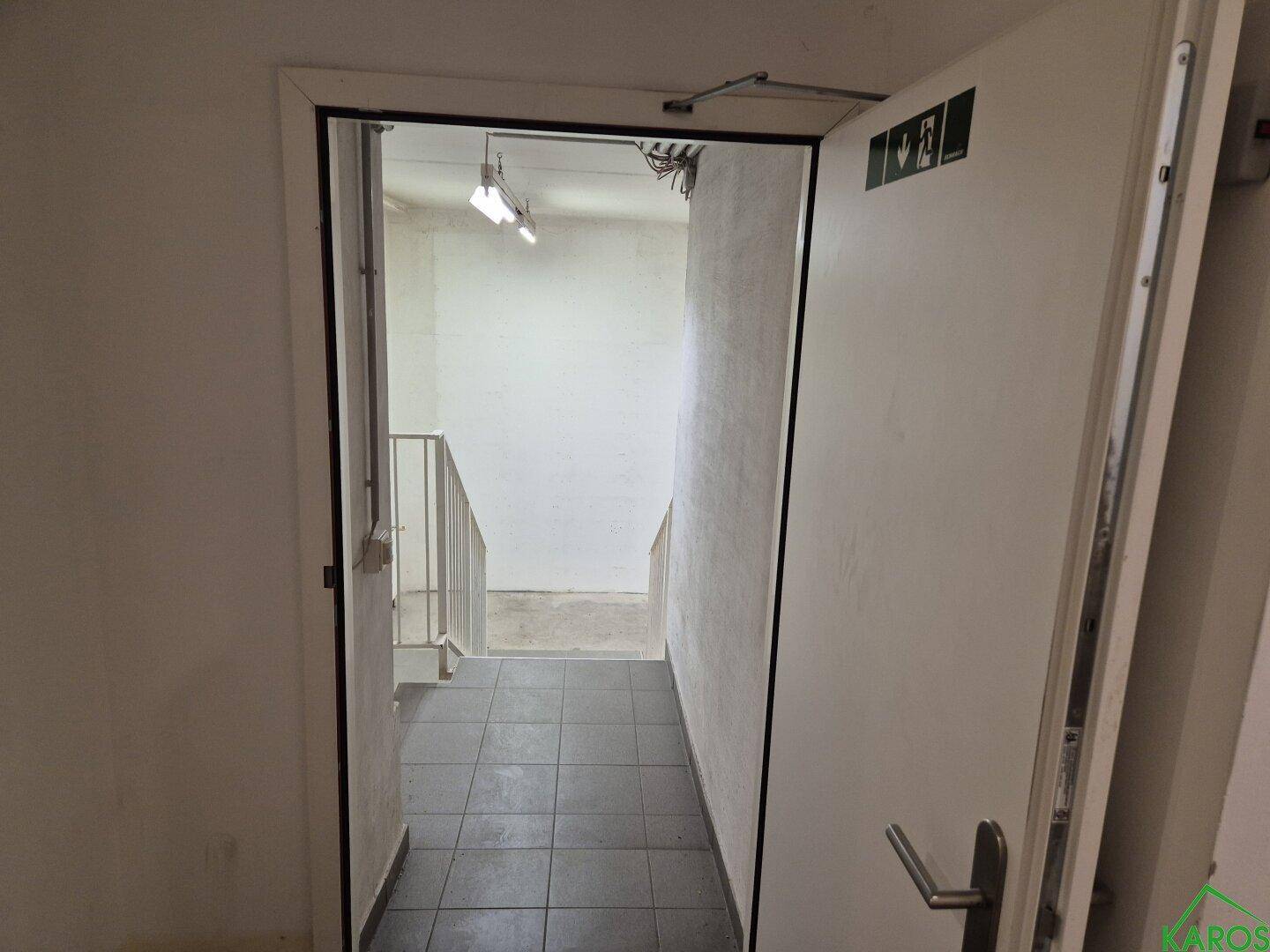 Treppenhaus mit dunklem Fliesenboden und einer Sicherheitstür, die in ein Untergeschoss führt.