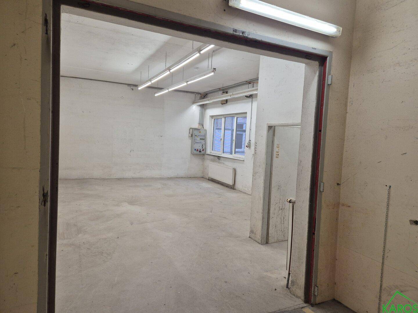 Leerer Raum mit Betonboden, weißen Wänden, Leuchtstoffröhren und Fenster, ideal als Lager oder Werkstatt.