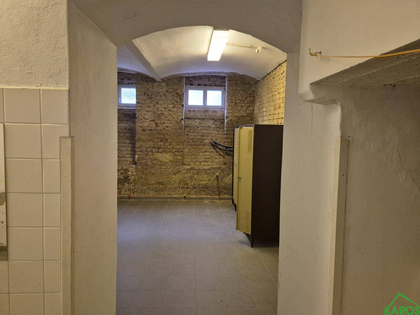 Kellerraum mit freigelegten Ziegelwänden, gefliestem Boden, Gewölbedecke und zwei kleinen Fenstern.