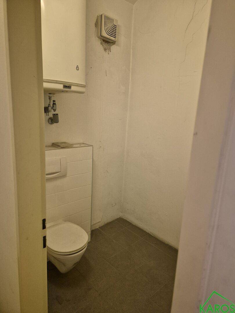 Kleine Toilette mit Wand-WC, Spülkasten und Abluftventilator, in einem einfachen Design gehalten.
