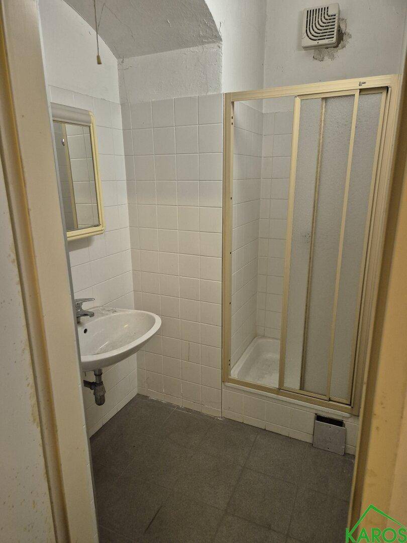 Badezimmer mit Duschkabine, Waschbecken und weißen Fliesen, ausgestattet mit Abluftventilator.
