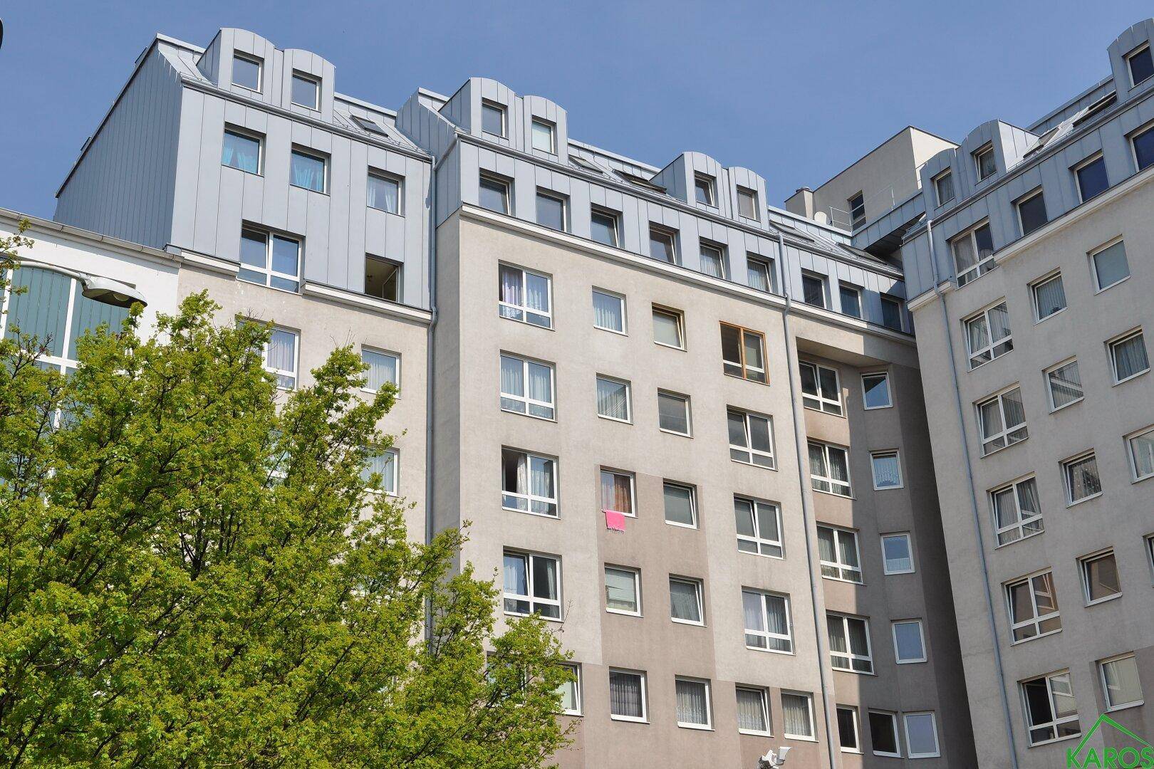 Mehrstöckiges Wohngebäude mit moderner Architektur und zahlreichen Fenstern unter blauem Himmel.