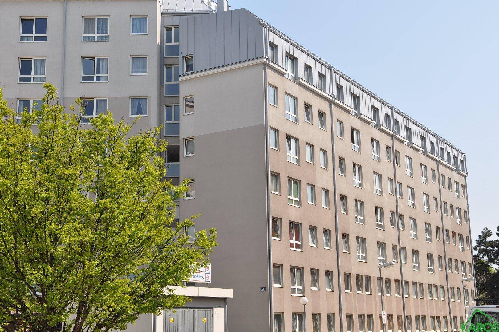 Ansicht eines großen Wohnkomplexes mit vielen Fenstern und einem Baum im Vordergrund.