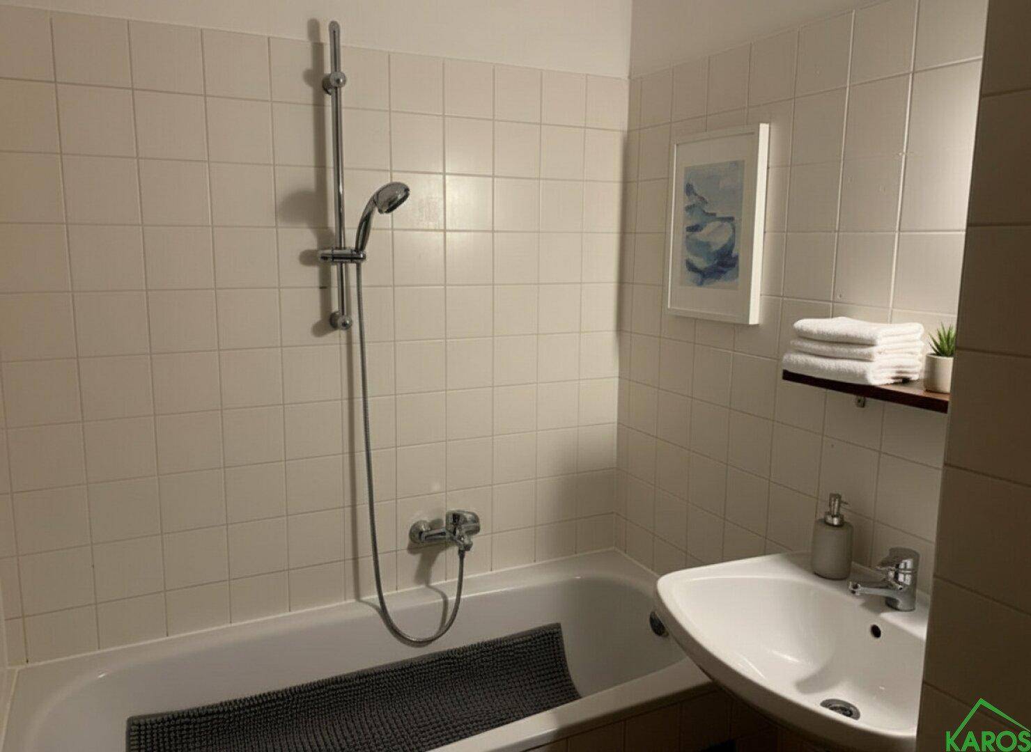 Helles Badezimmer mit Badewanne, Duscharmatur und Waschbecken, komplett gefliest.