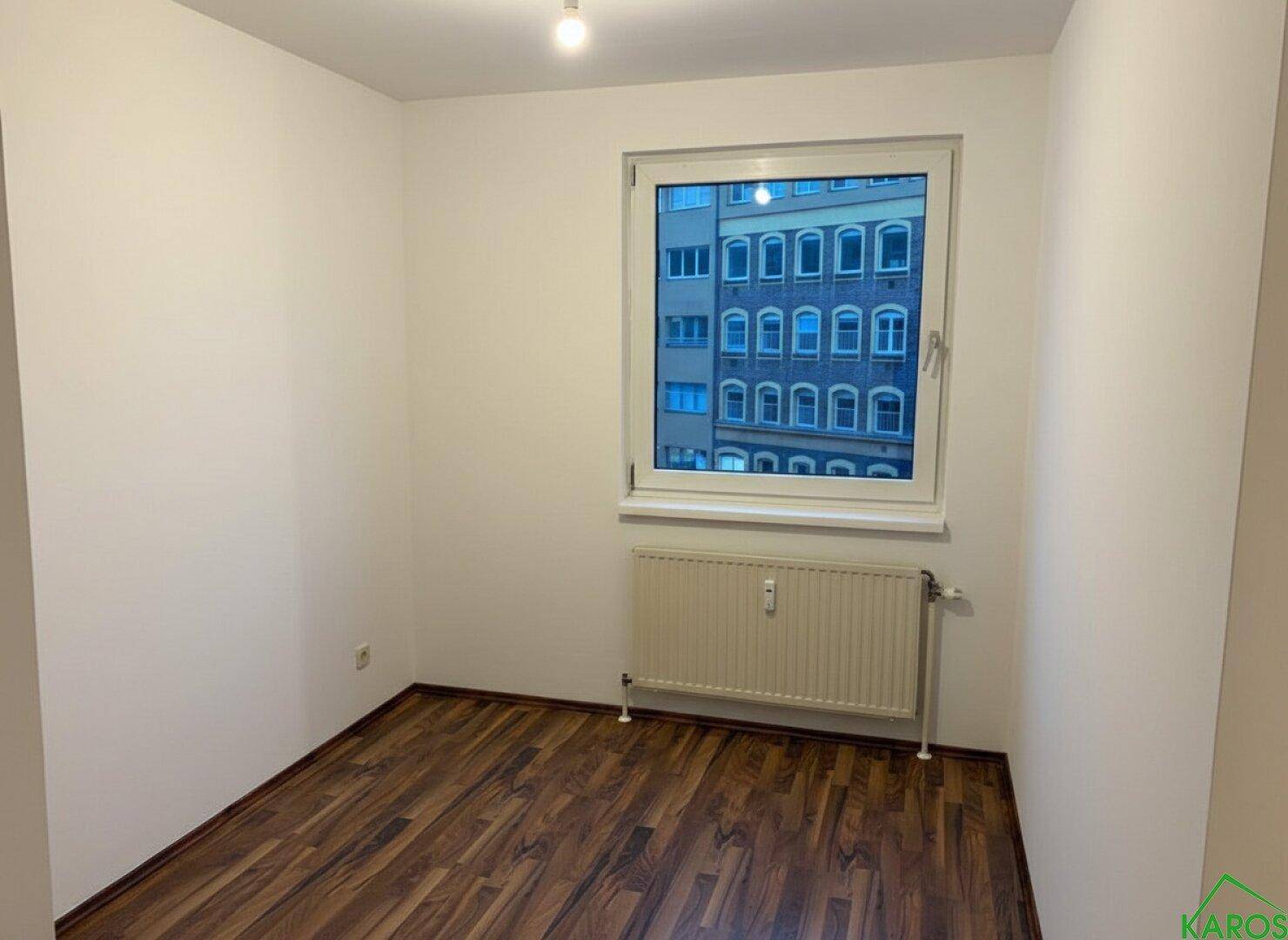 Unmöbliertes Schlafzimmer mit Laminatboden und einem Fenster mit Stadtblick.