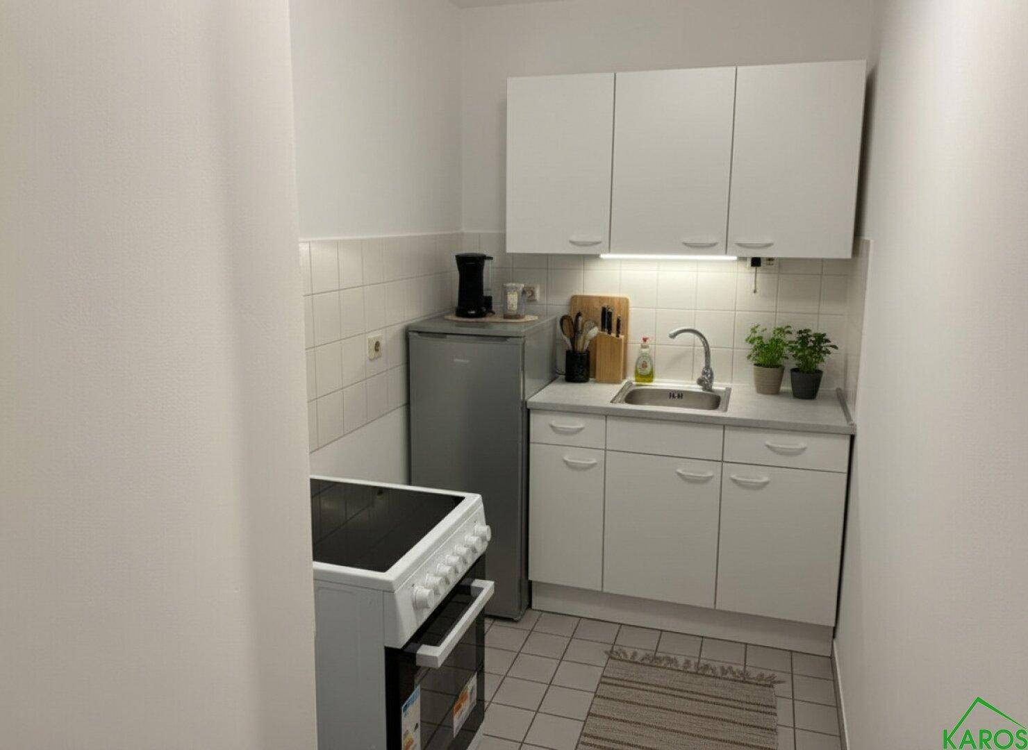 Kompakte Küchenzeile mit weißen Schränken, Spüle, Herd und Kühlschrank.