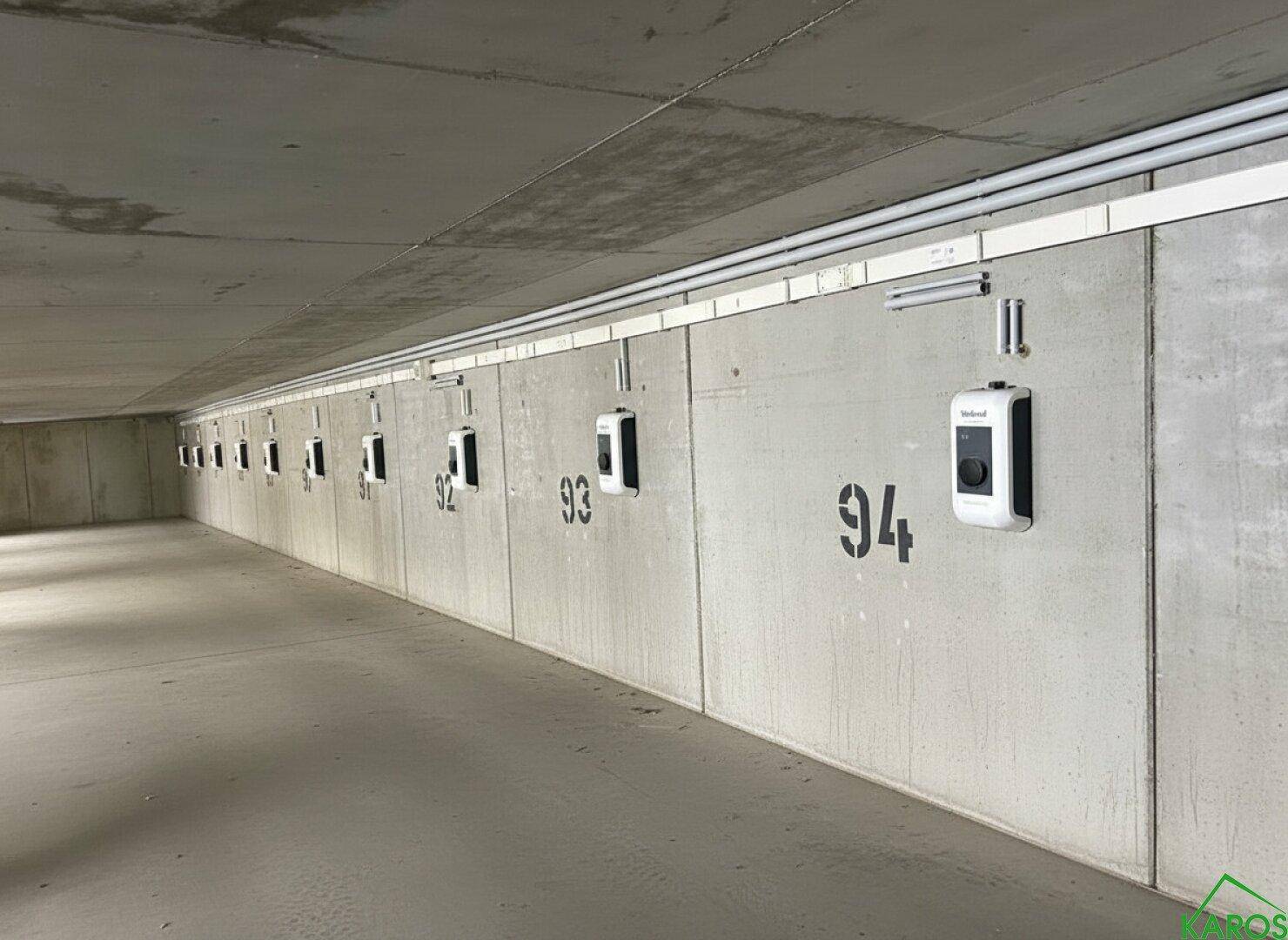Innenansicht eines Parkhauses mit einer Reihe von modernen Ladestationen für Elektrofahrzeuge an der Betonwand.