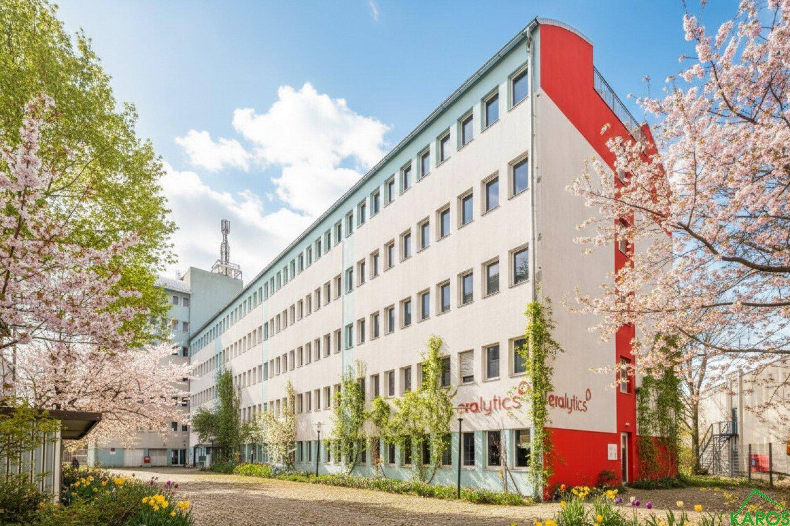 Modernes Bürogebäude mit weißer Fassade, roten Akzenten und blühenden Bäumen im Frühling.