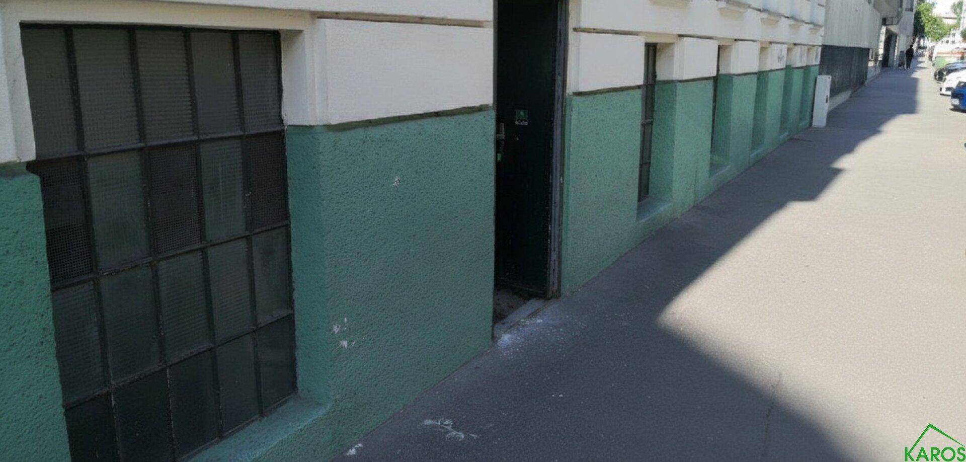 Außenansicht eines Gebäudes mit grün gestrichener Fassade, vergitterten Fenstern und einem offenen Eingangsbereich.
