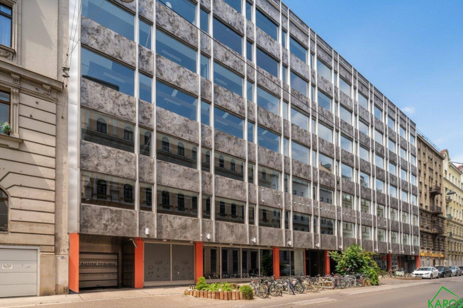 Moderne Bürogebäude-Fassade mit großen Glasflächen und Betonverkleidung, umgeben von städtischer Architektur.