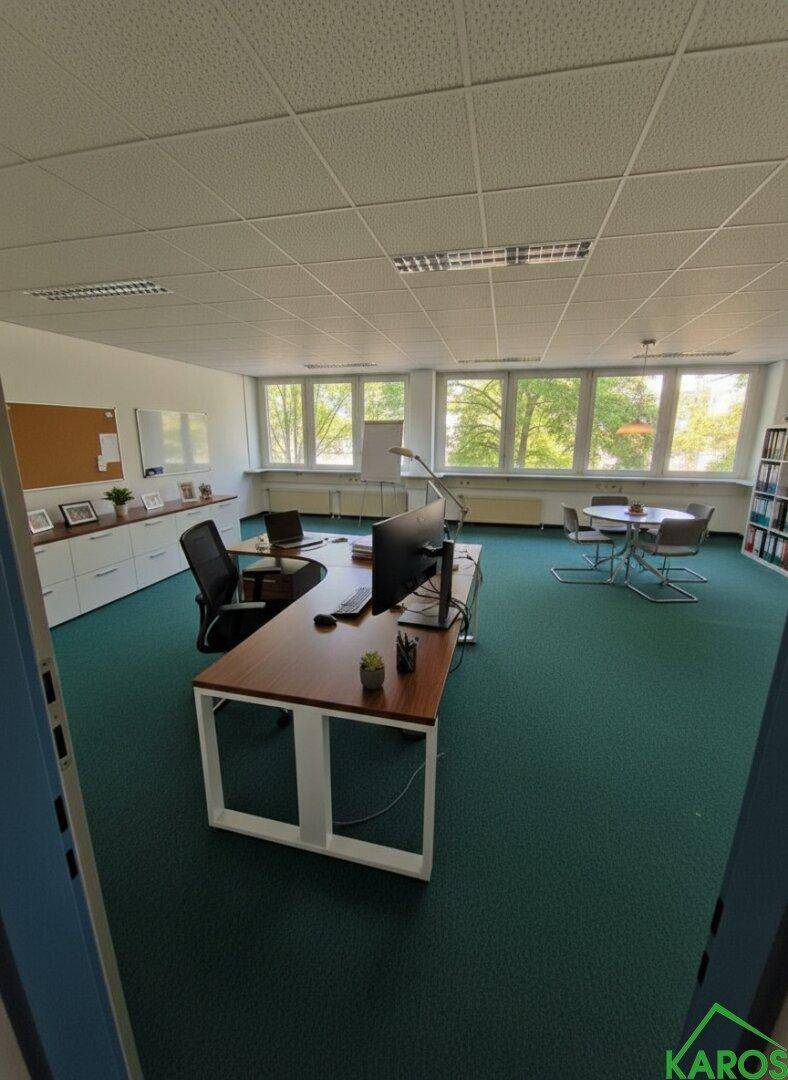 Büro mit mehreren Arbeitsplätzen, grünem Teppichboden und Blick auf die umliegende Natur durch die Fenster.