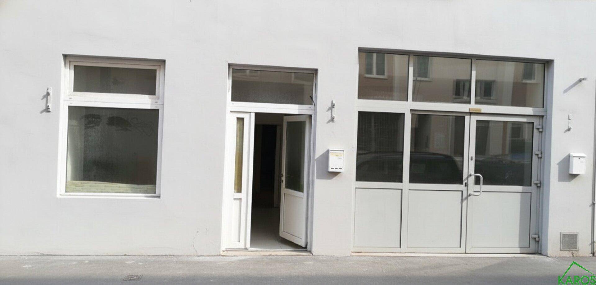 Helle Fassade mit großem Fenster, Eingangstür und einer breiten Glasfront, die als Garagentor dient.