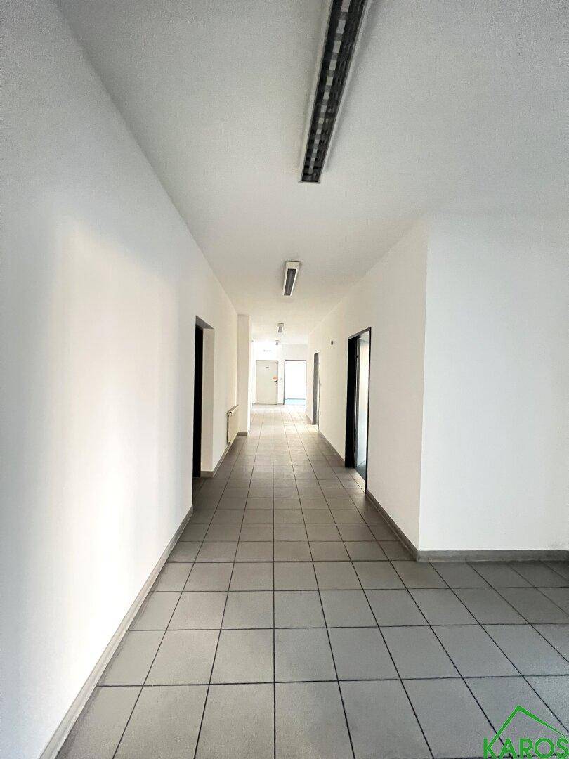 Langer, heller Flur mit Fliesenboden und weißen Wänden, der zu mehreren Büroräumen führt.