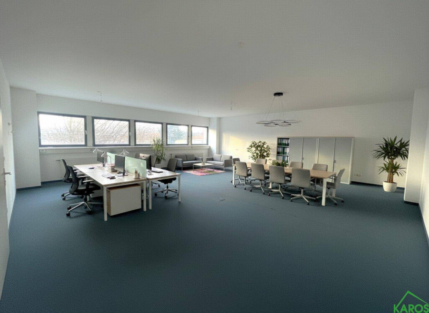 Großes, offenes Büro mit mehreren Arbeitsplätzen, Konferenztisch und Fenstern entlang der Wand.