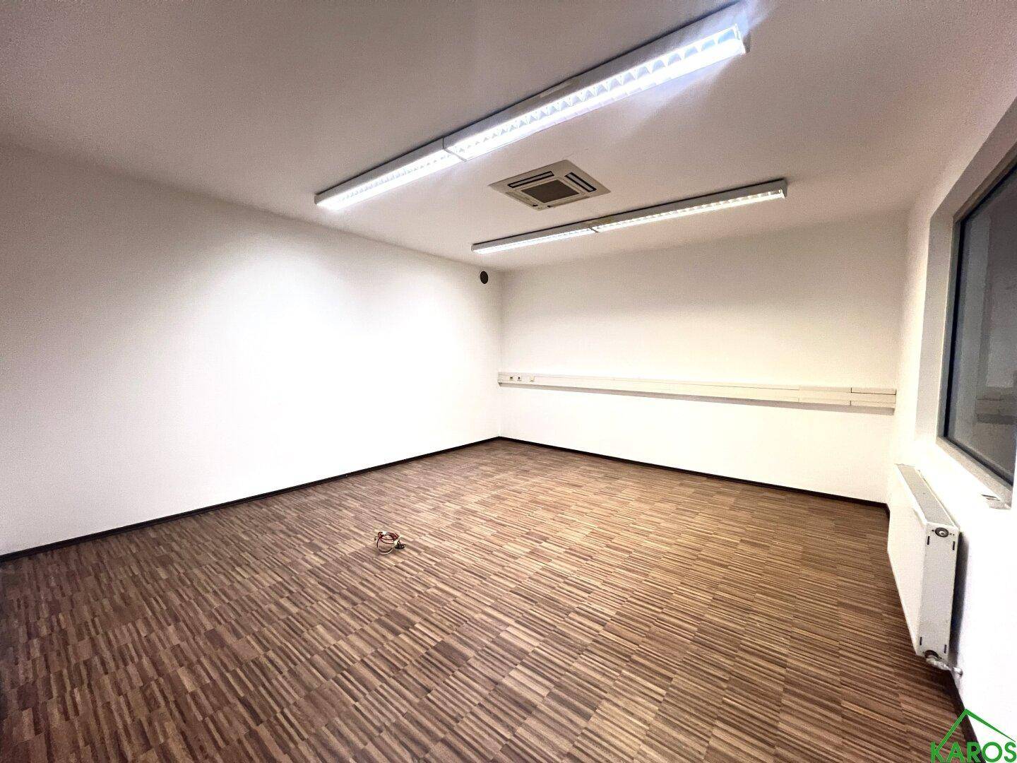 Leeres Büro mit Holzboden, weißen Wänden und Deckenbeleuchtung, bereit zur individuellen Gestaltung.