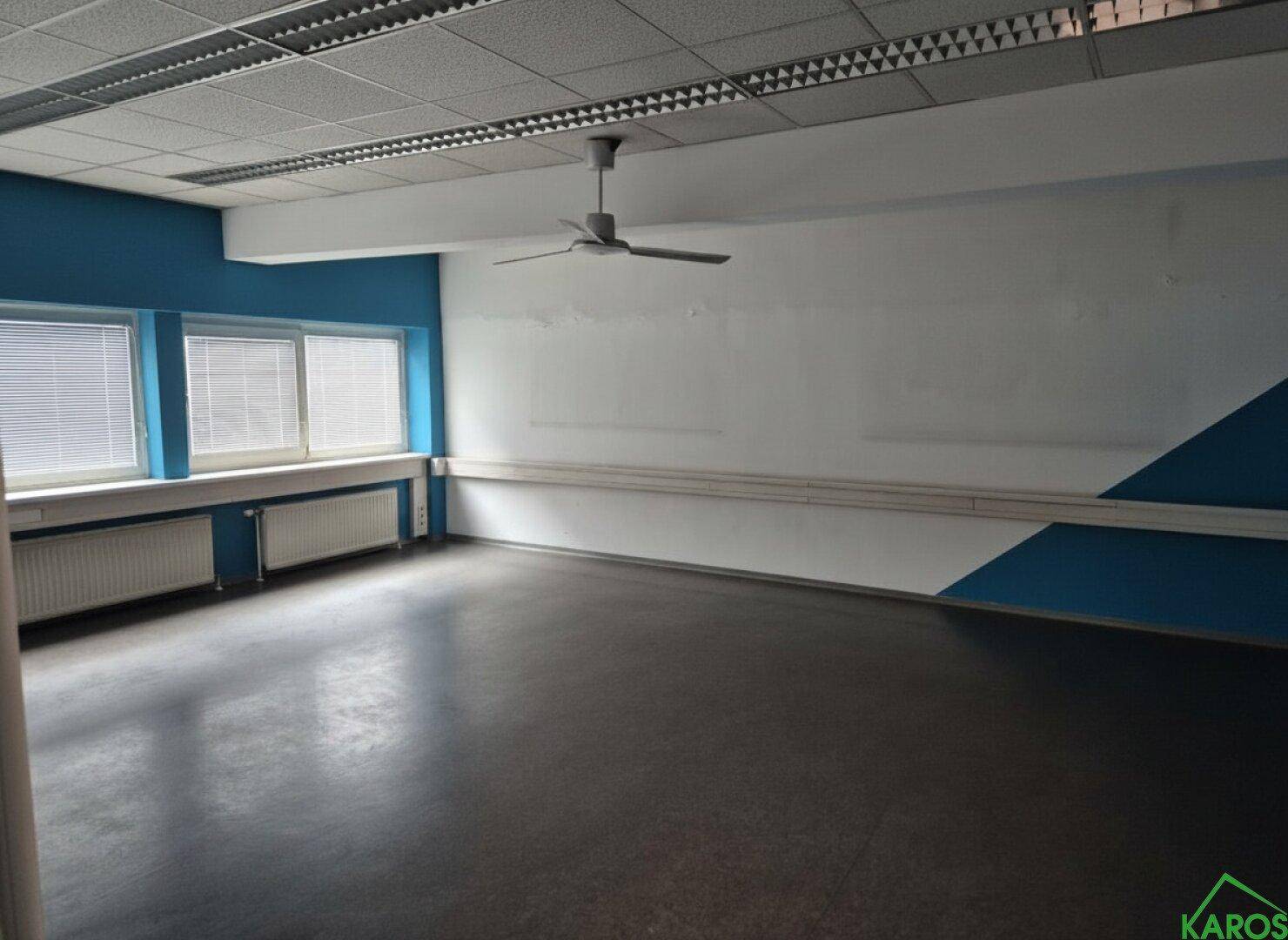 Leeres Büro mit blauen Akzentwänden, großen Fenstern und einem Deckenventilator, bereit zur individuellen Gestaltung.