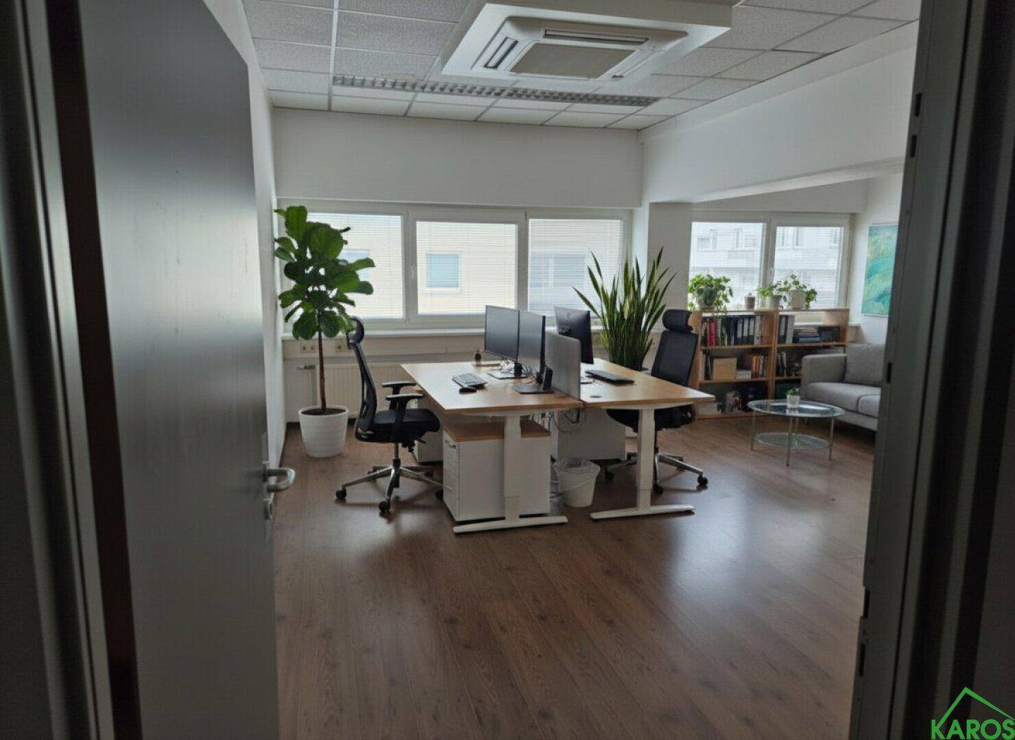 Helles Büro mit Holzboden, mehreren Arbeitsplätzen und einer gemütlichen Sitzecke, ideal für kreative Teams.