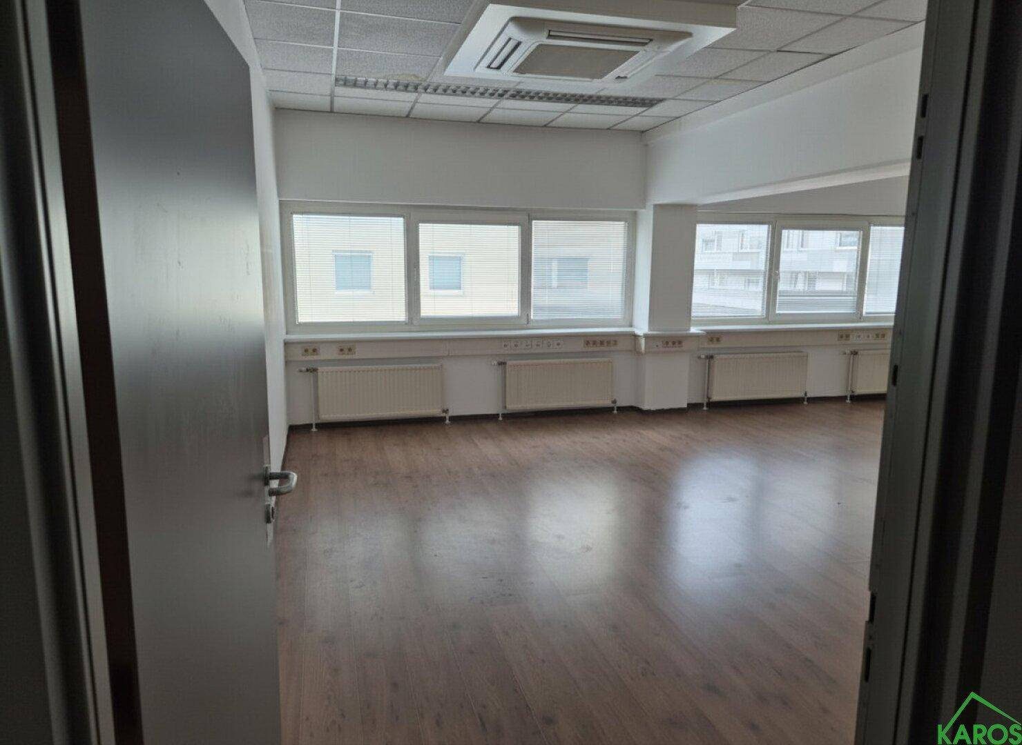 Leeres Büro mit warmem Holzboden und großen Fenstern, bietet viel Potenzial für eine individuelle Einrichtung.