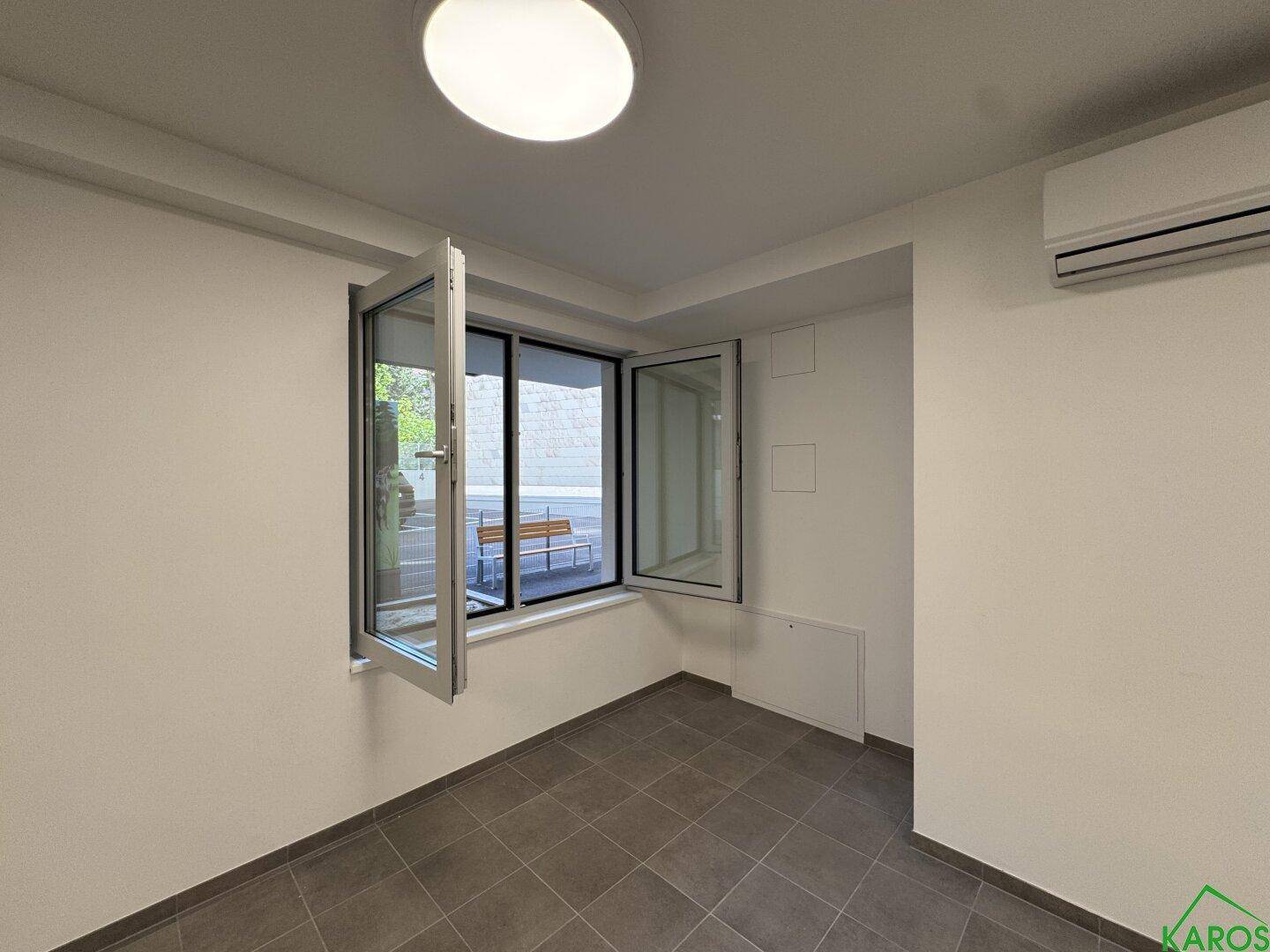 Helle Ecke eines Büroraums mit geöffnetem Fenster, das Tageslicht hereinlässt, und einer installierten Klimaanlage.