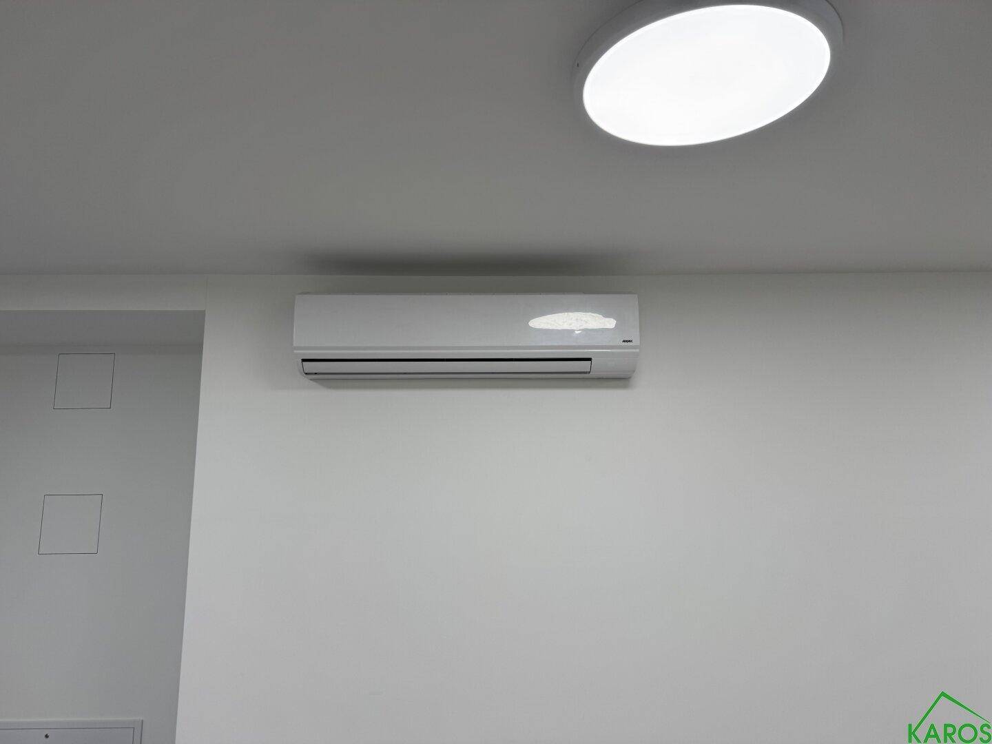 Nahaufnahme einer modernen Klimaanlage an einer weißen Wand unter einer runden Deckenleuchte.