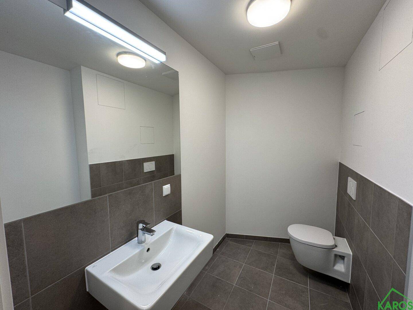 Helles Badezimmer mit modernem Design, wandhängendem WC, Waschbecken und großem Spiegel über den Fliesen.