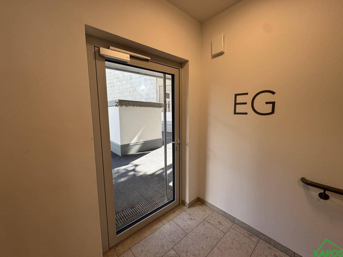 Heller Eingangsbereich mit einer Glastür, die nach draußen führt, und der Beschriftung "EG" an der Wand.
