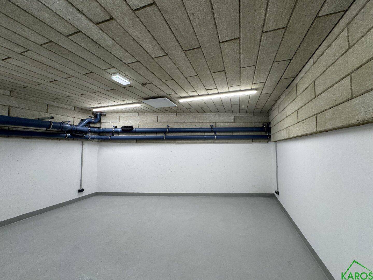 Kellerraum mit sichtbaren blauen Rohren an der Decke und einem grauen Boden, ideal als Lagerfläche.