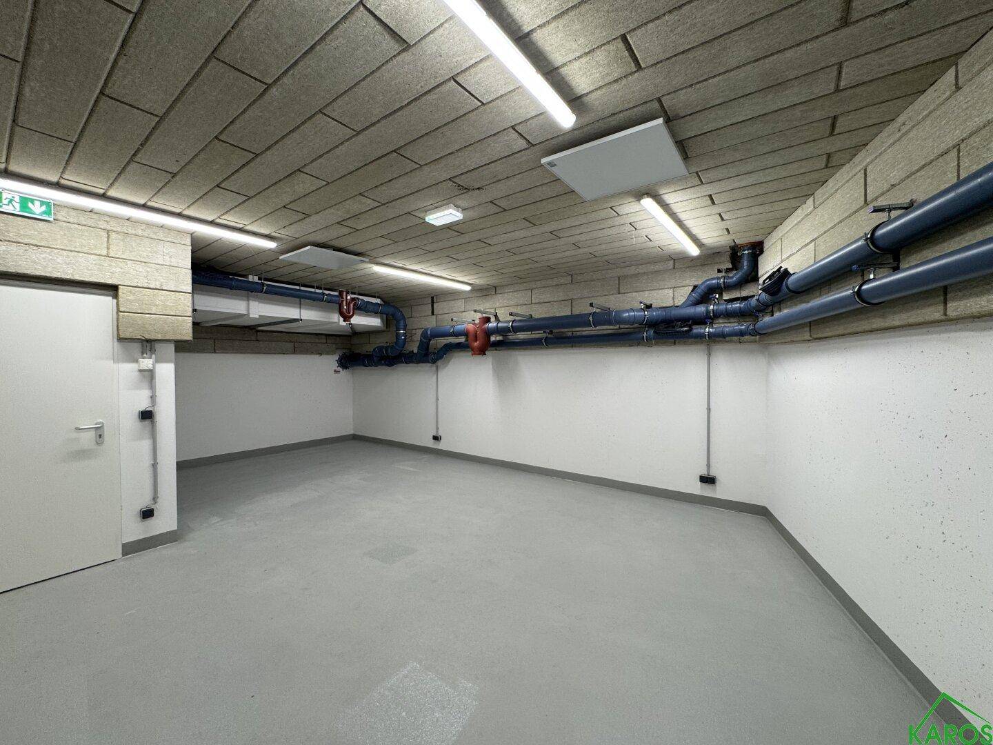 Leerer Kellerraum mit sichtbaren Versorgungsleitungen und robustem Bodenbelag in einem Neubau.