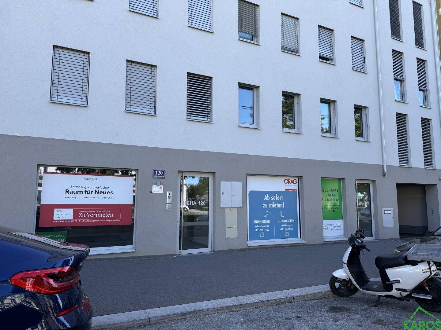 Moderne Gebäudefassade mit Geschäftsflächen im Erdgeschoss und Wohnungen darüber, an einer Straße gelegen.