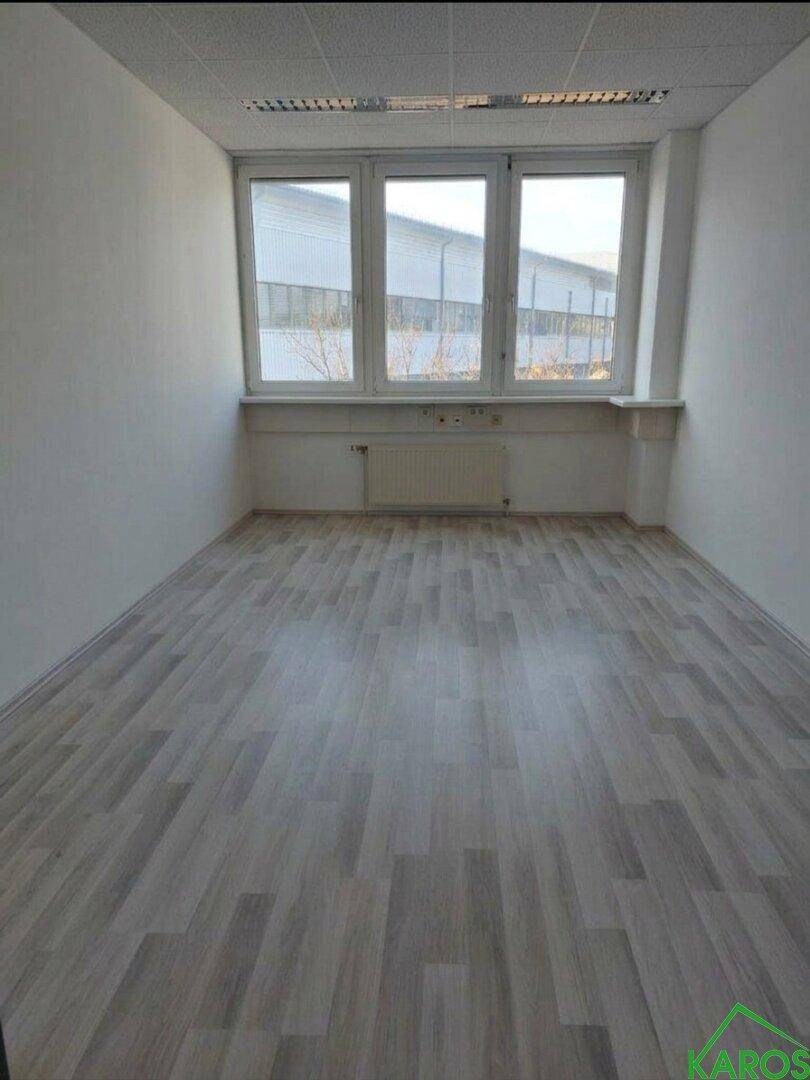 Leerer Büroraum mit großen Fenstern, Heizkörper und hellem Laminatboden, bereit zur individuellen Gestaltung.