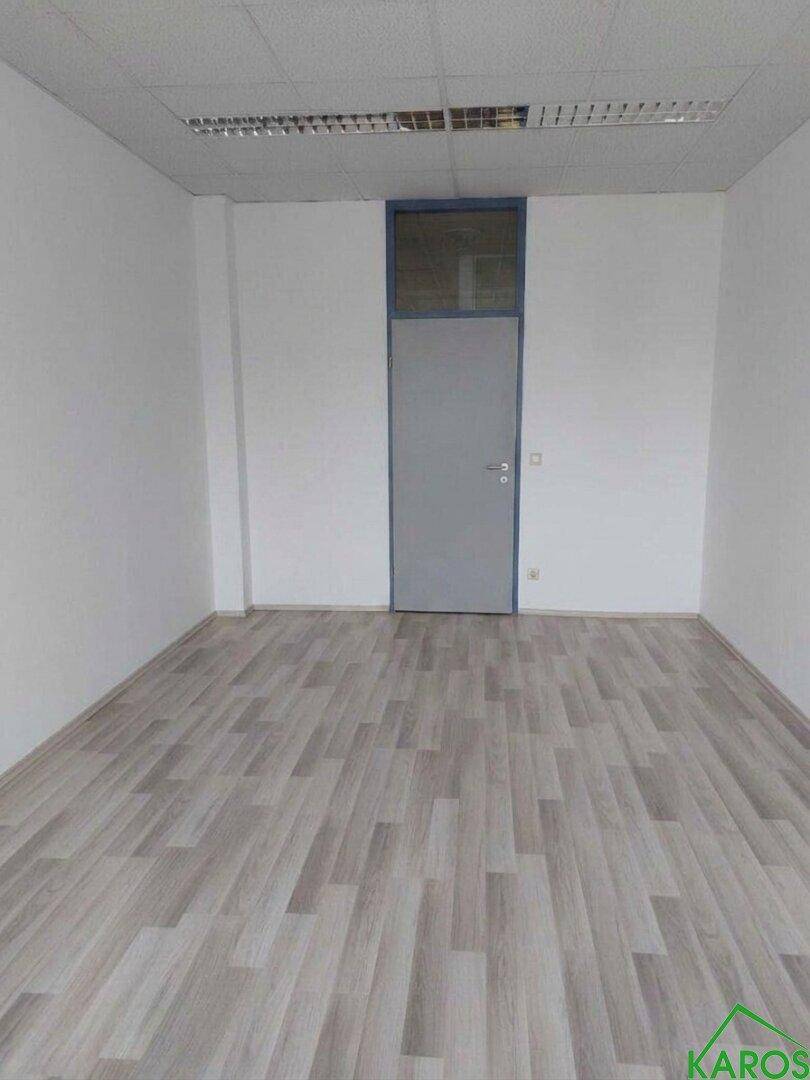 Leerer Büroraum mit einer Tür und hellem Laminatboden, ideal für flexible Bürolösungen.