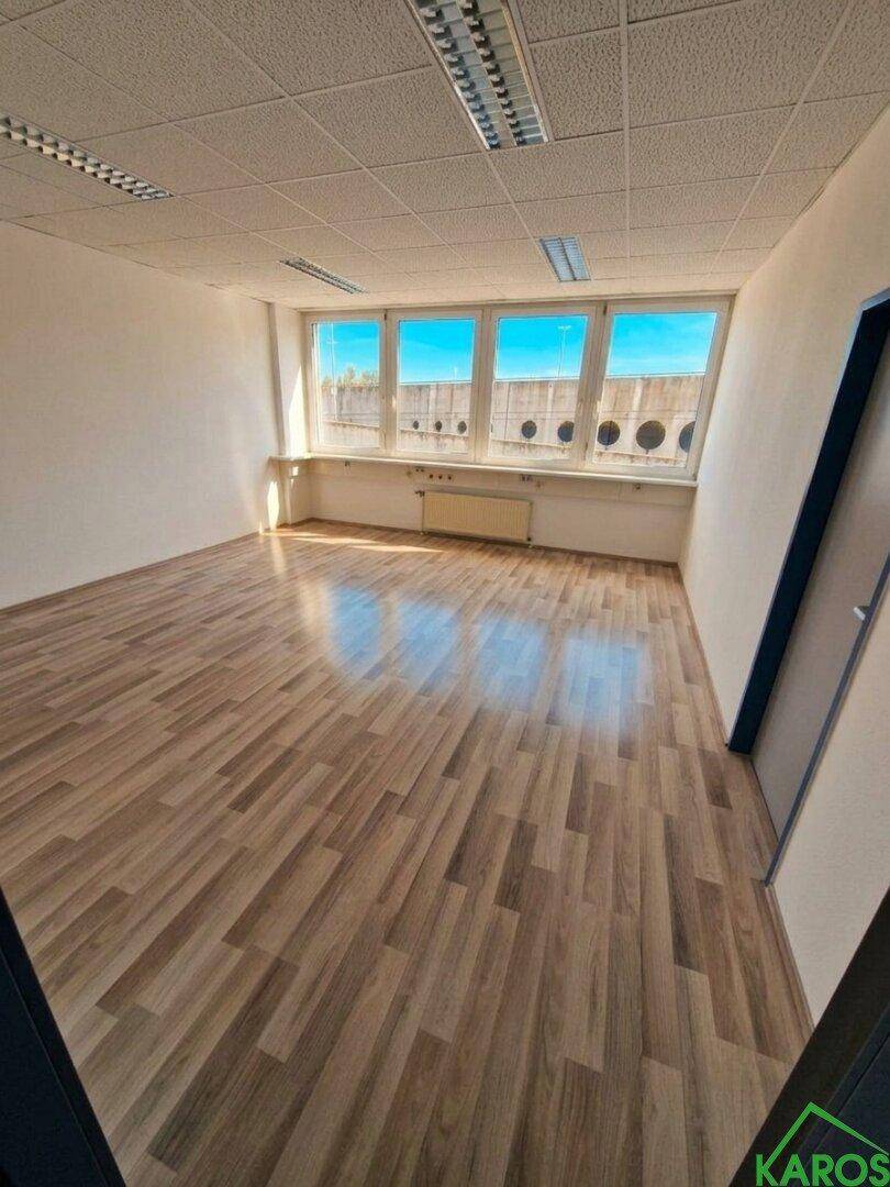 Leeres Büro mit Laminatboden und großen Fenstern, bereit für die individuelle Einrichtung.