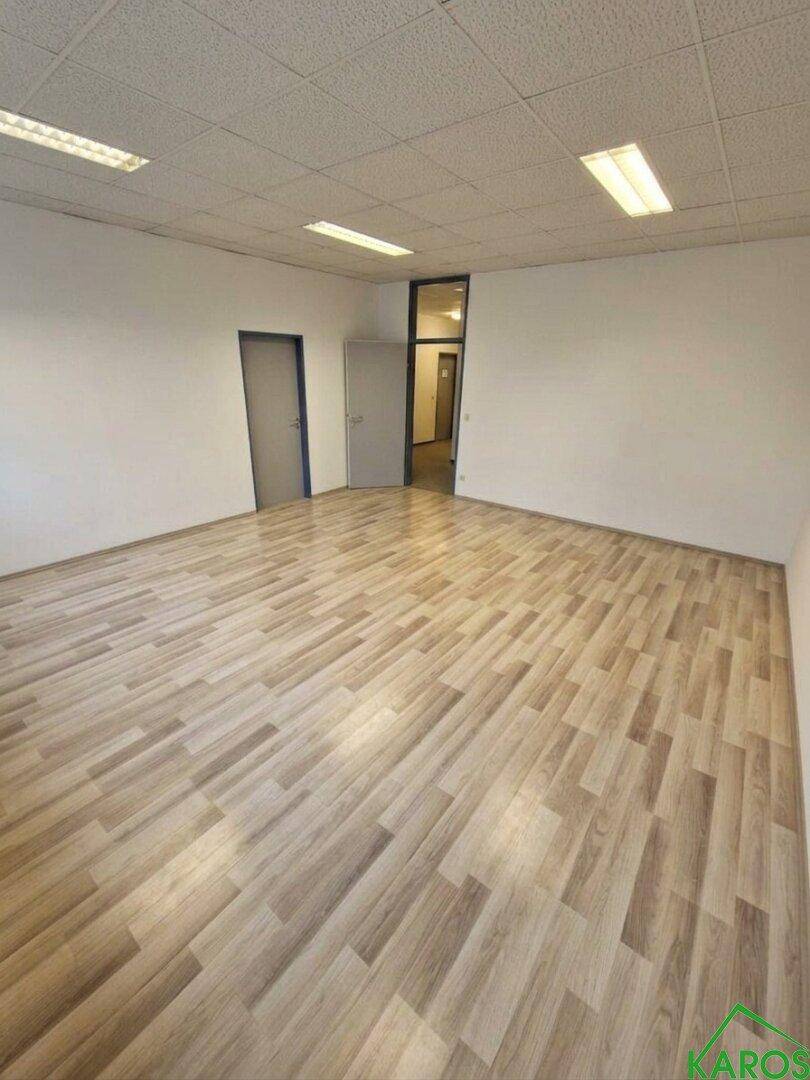 Leerer Büroraum mit Laminatboden und weißen Wänden, ideal für flexible Gestaltungsmöglichkeiten.