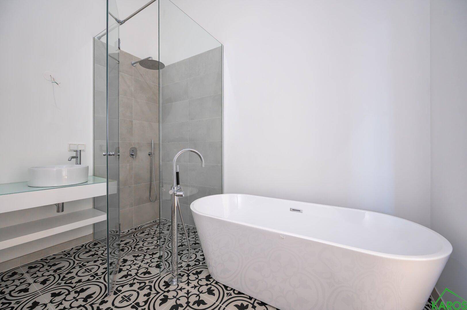 Modernes Badezimmer mit freistehender Badewanne, begehbarer Dusche und auffälligen gemusterten Bodenfliesen.