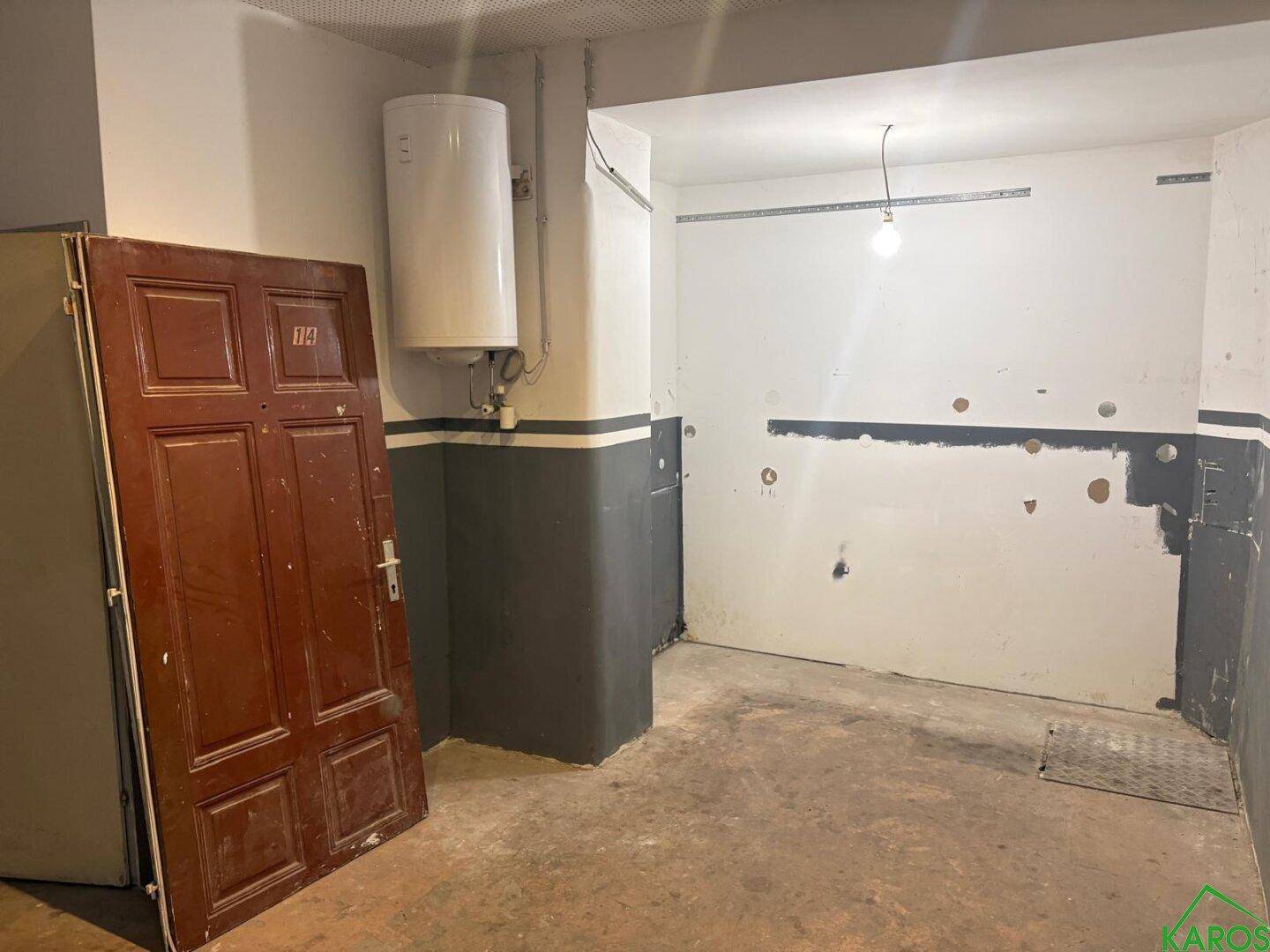Einfacher Hauswirtschaftsraum mit Warmwasserbereiter, Betonboden und Renovierungsbedarf.