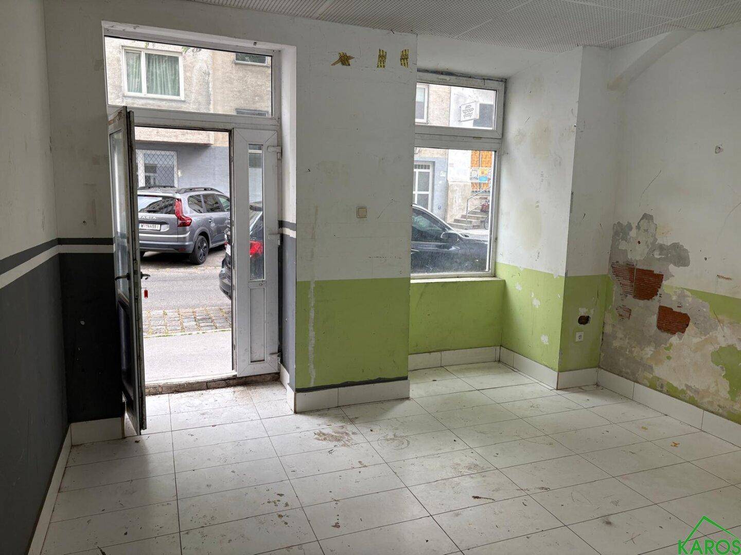 Erdgeschossraum mit Fliesenboden, Renovierungsbedarf und direktem Zugang zur Straße.