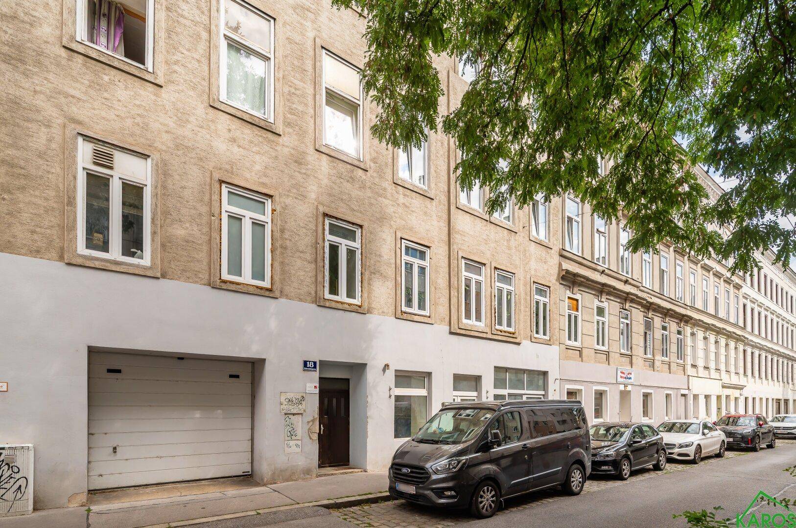 Fassade eines Mehrfamilienhauses mit Garagentor und parkenden Autos auf der Straße.