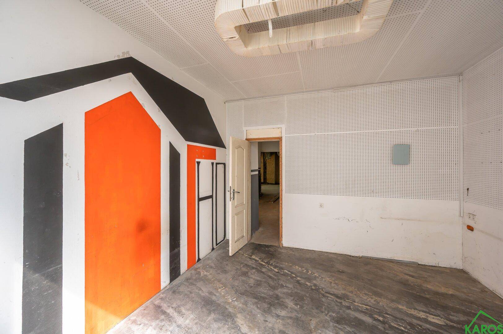 Offener Raum mit perforierter Decke, Betonboden und auffälliger Wandmalerei.