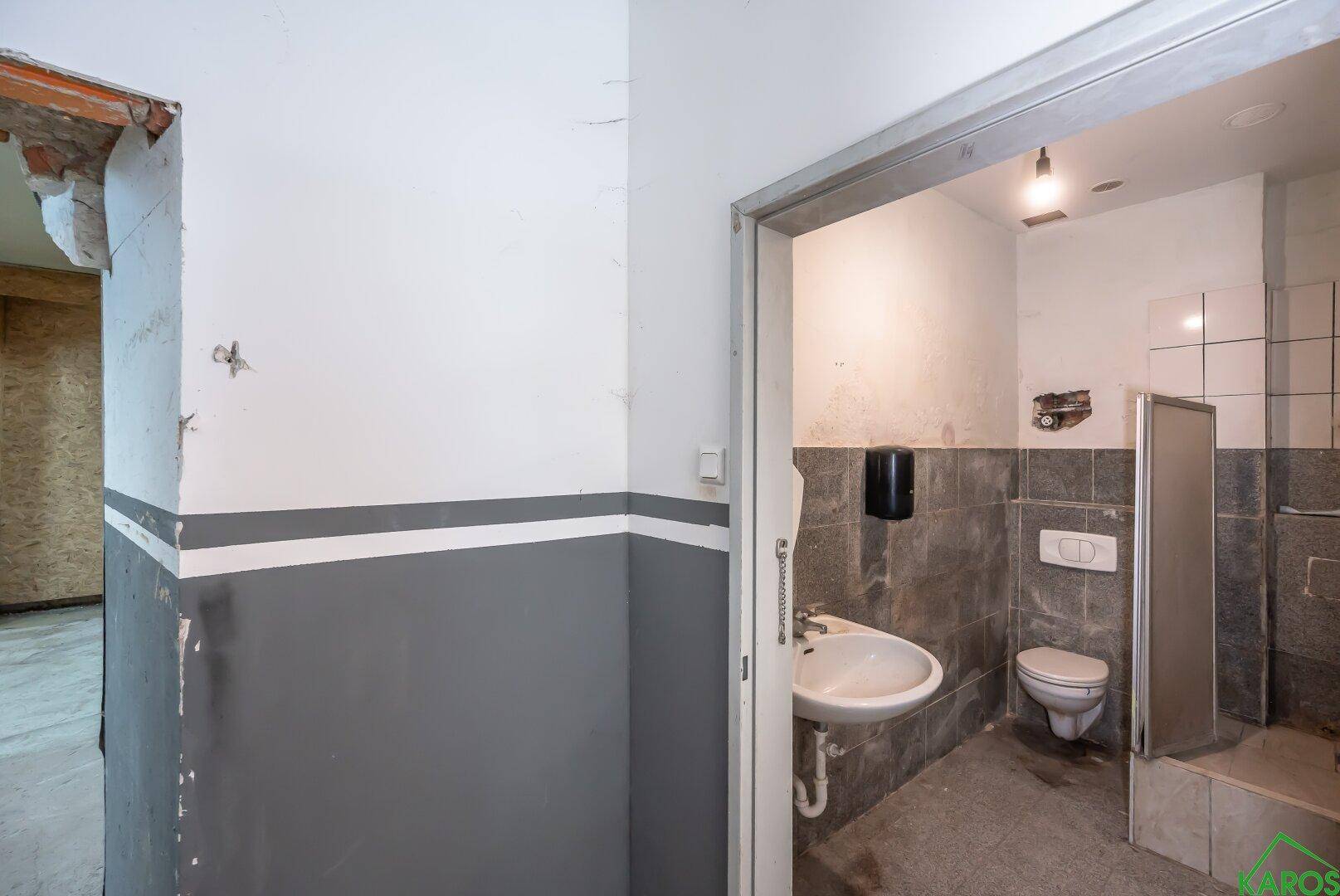 Einfache Toilette mit Waschbecken, gefliesten Wänden und Betonboden.