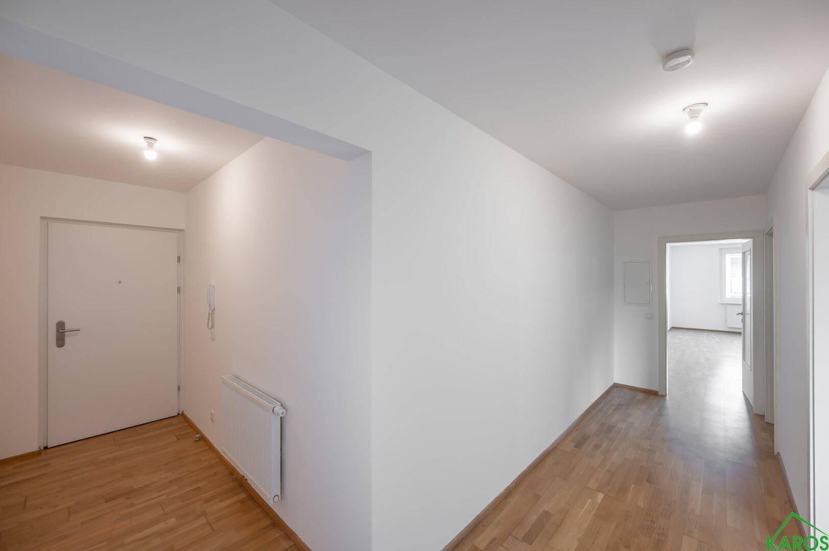Heller Eingangsbereich einer Wohnung mit Holzparkettboden und weiß gestrichenen Wänden.