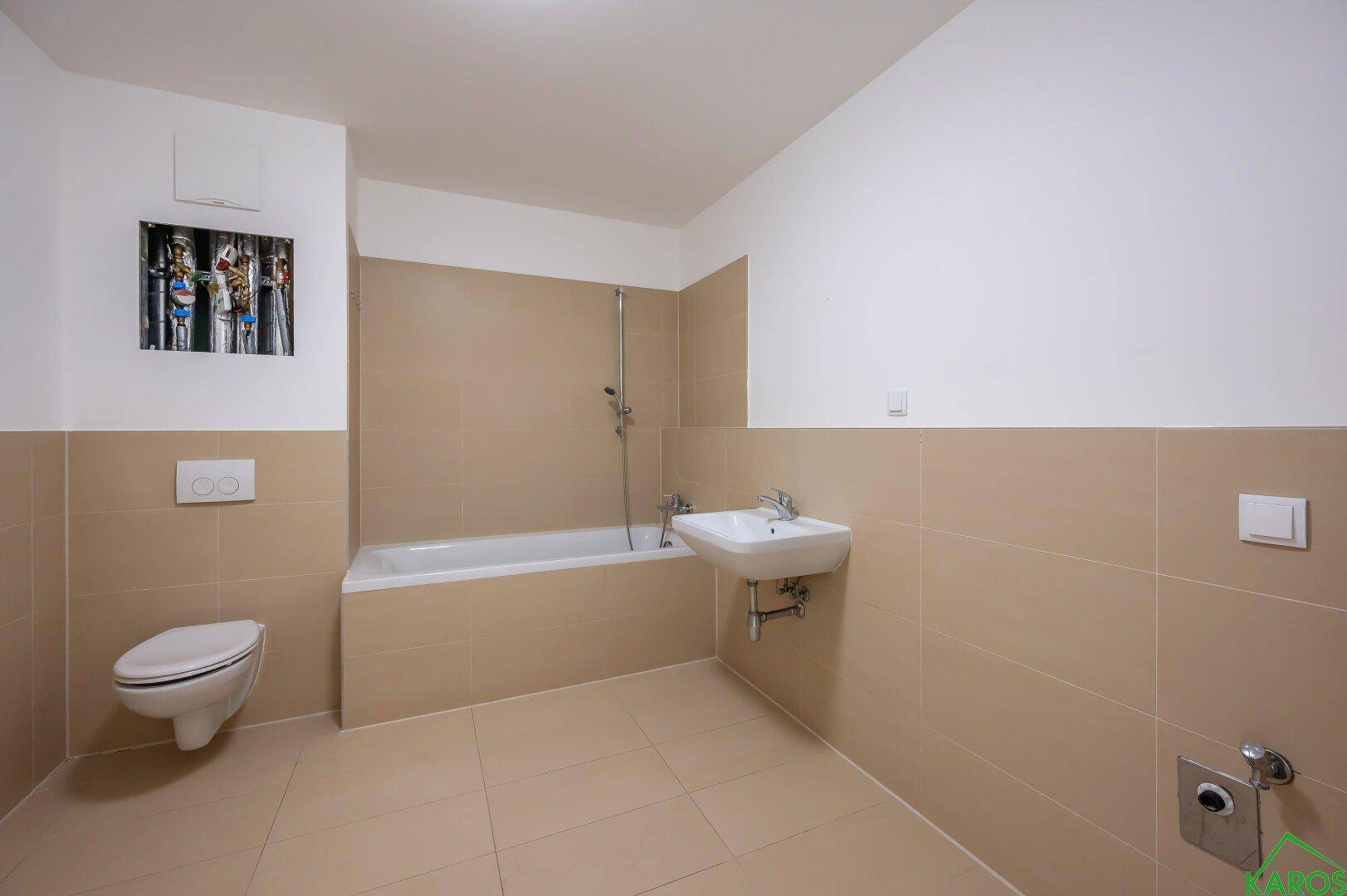 Badezimmer mit beigefarbenen Fliesen, Badewanne, Toilette und Waschbecken.