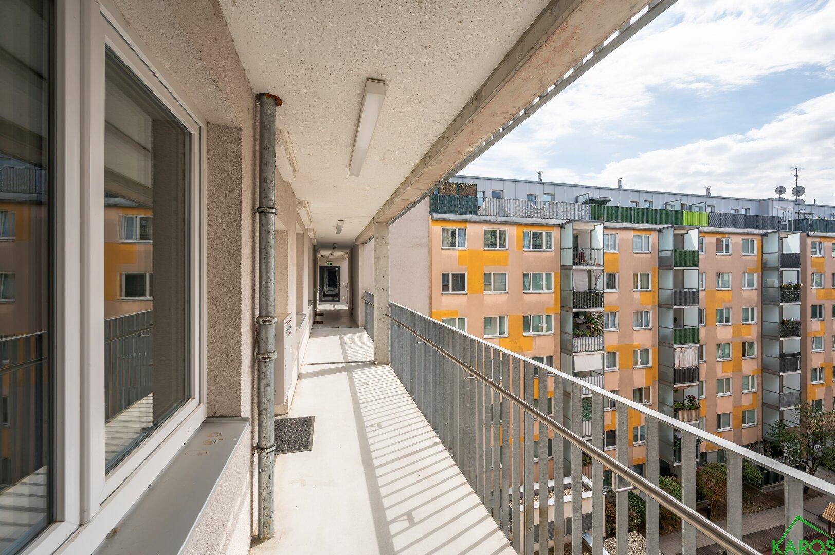 Langer, überdachter Balkon mit Geländer und Blick auf die umliegenden Wohngebäude.