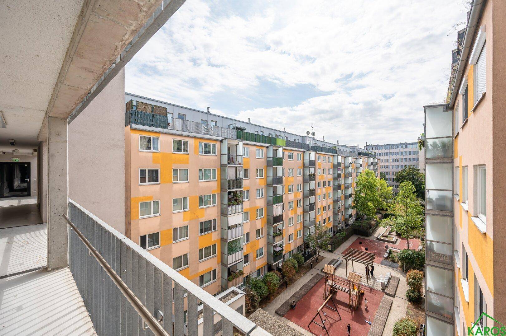 Blick vom Balkon auf einen Innenhof mit Spielplatz und weiteren Wohngebäuden.